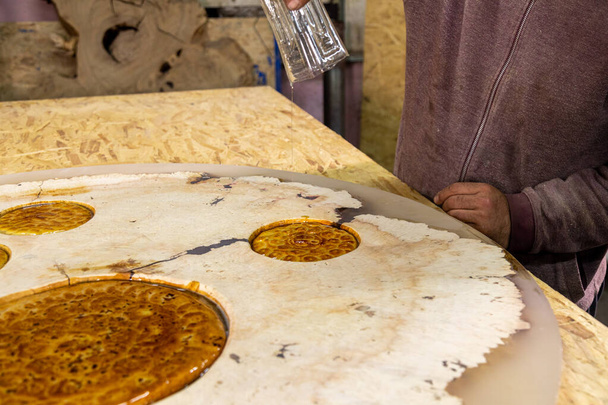 Closeup of carpenter pouring liquid epoxy on a wooden round table decorated with flatbreads. Creative epoxy table design - Valokuva, kuva