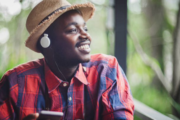 笑顔アフリカの旅行者は喜んで自分のスマートフォンで美しい音楽を聞いています。テクノロジーの概念と日々の幸福 - 写真・画像
