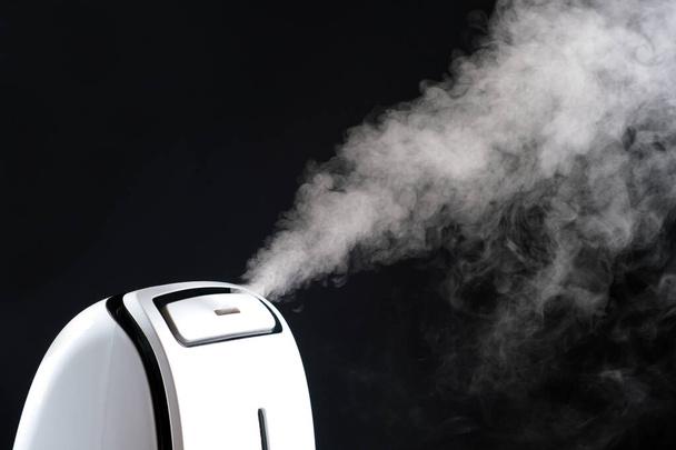 Humidifier with steam jet on a black background. Humidity in the room, maintaining the microclimate in the apartment. - Photo, Image
