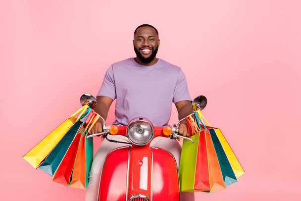 Photo of funny cheerful guy wear purple t-shirt riding moped carrying shoppers isolated pink color background - Φωτογραφία, εικόνα