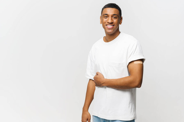 Portrait of happy young African American guy showing arm with patch-aid after coronavirus vaccine - Fotografie, Obrázek