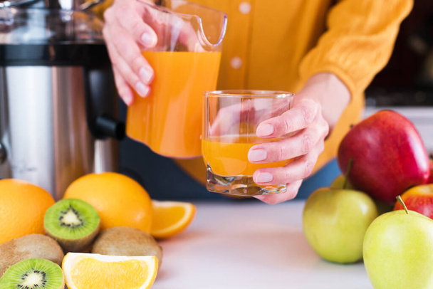 Woman's hands pour freshly squeezed fruit juice into a glass. Natural and healthy juices at home. Close-up. Selective focus. - Fotoğraf, Görsel