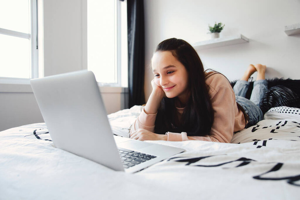 Nice teenage girl using a computer in her bedroom. - Фото, изображение