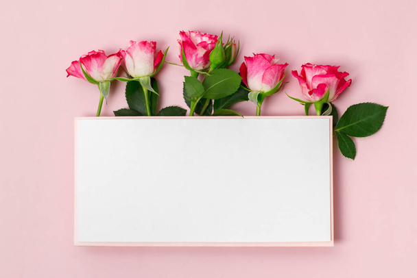 Composition with delicate pink rose flowers and blank paper on a pastel pink background. Greetind card mockup. - Photo, image