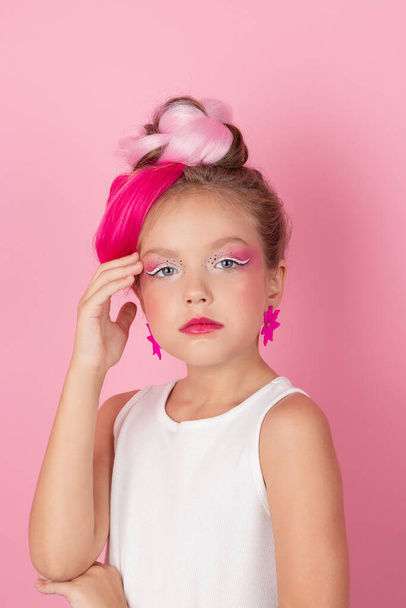 чарівна маленька дівчинка з рожевою зачіскою і рожевим макіяжем. між молодою моделлю позує на рожевому фоні
. - Фото, зображення