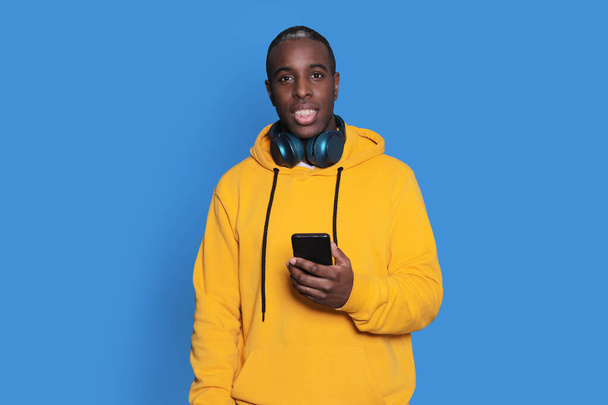Cheerful African American man in yellow sweater using mobile phone application. - Foto, afbeelding