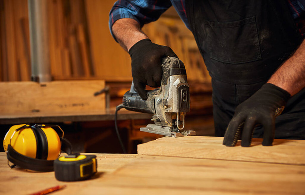 Close up of professional carpenter hands sawing wood with an electric jigsaw in the carpentry workshop - Foto, Imagem