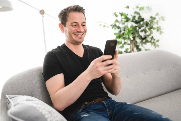 A european man using his phone on the living room - Fotoğraf, Görsel