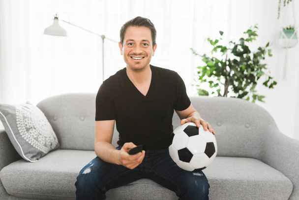 A portrait at home of excited man watching European football game on TV celebrating goal on couch - Fotoğraf, Görsel