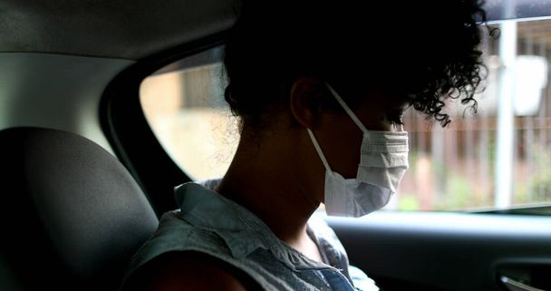 Passenger girl in backseat taxi wearing pandemic virus mask looking at smartphone - Photo, Image