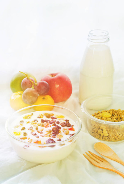 Grains Granola in a glass milk bottle and fruit on a white cloth in the morning sunlight. - Photo, Image