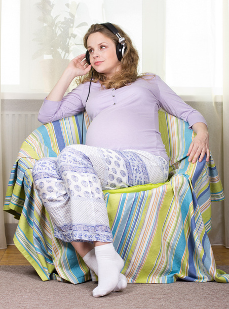 Krásná těhotná blondýna poslouchá klasickou hudbu na sluchátka. Portrét těhotné ženy. Vývoj dítěte v děloze - Fotografie, Obrázek