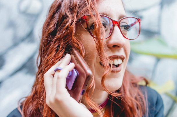 close up beautiful young redhead woman with glasses, outdoors talking on the phone and laughing. - Fotografie, Obrázek