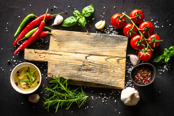 Food background. Oak cutting board, spices and vegetables at kitchen table. - Fotó, kép