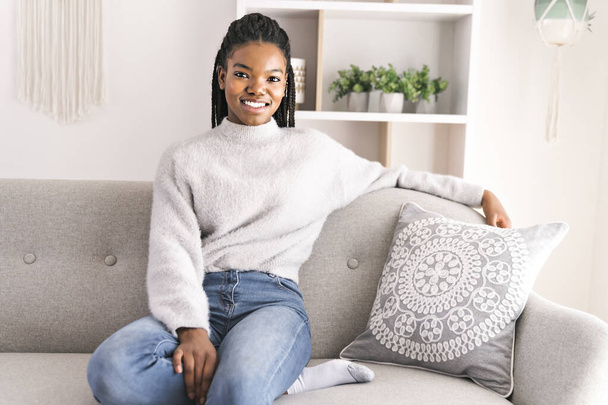 Young African American teen on a sofa in her living room relaxing - Fotó, kép