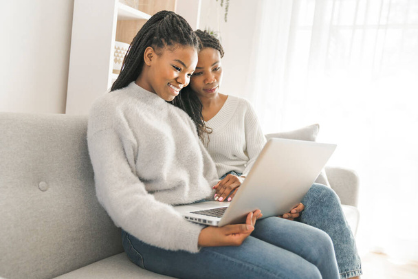 Mother and daughter sitting on sofa at home with laptop - Photo, image