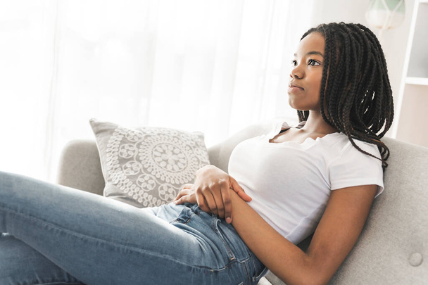 Young African American teen relaxing on a sofa in her living room - Photo, Image