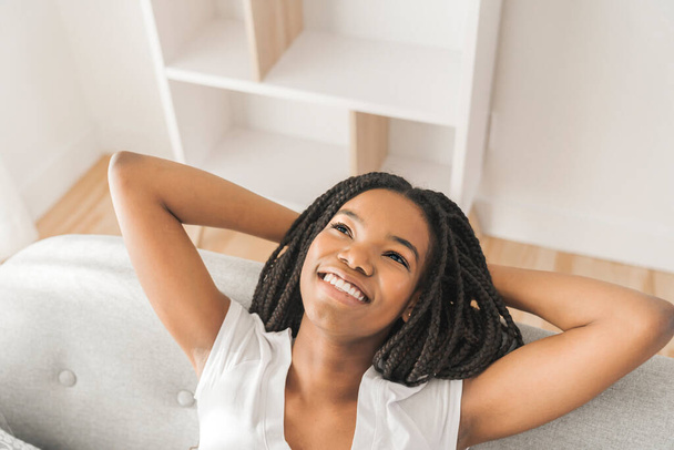 Young African American teen on a sofa in her living room relaxing - Фото, изображение