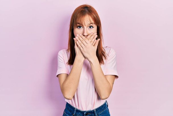 Pelirroja joven mujer usando casual rosa camiseta impactado cubriendo la boca con las manos por error. concepto secreto.  - Foto, Imagen