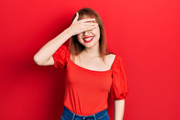 Redhead young woman wearing casual red t shirt smiling and laughing with hand on face covering eyes for surprise. blind concept.  - Valokuva, kuva