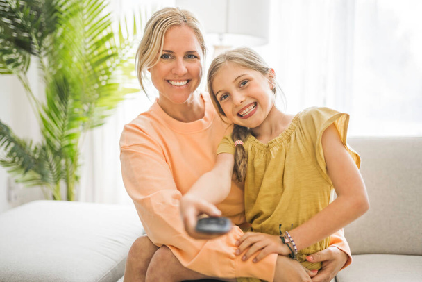 Cute child girl with his young mother at home watching tv - Valokuva, kuva
