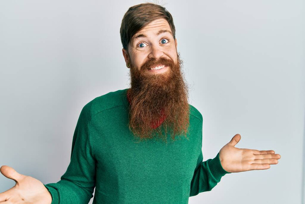 Uomo dai capelli rossi con la barba lunga che indossa abiti casual espressione indiscreta e confusa con braccia e mani sollevate. concetto di dubbio.  - Foto, immagini