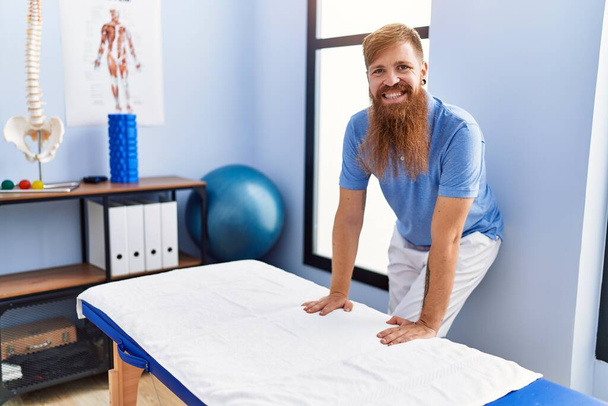Fiatal vörös hajú férfi fizioterapeuta egyenruhát visel a fizioterápiás klinikán. - Fotó, kép