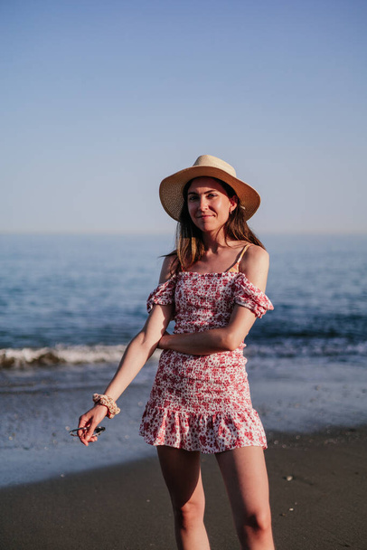 Portrét krásné mladé ženy s širokou krempou klobouku na pláži při západu slunce - Fotografie, Obrázek