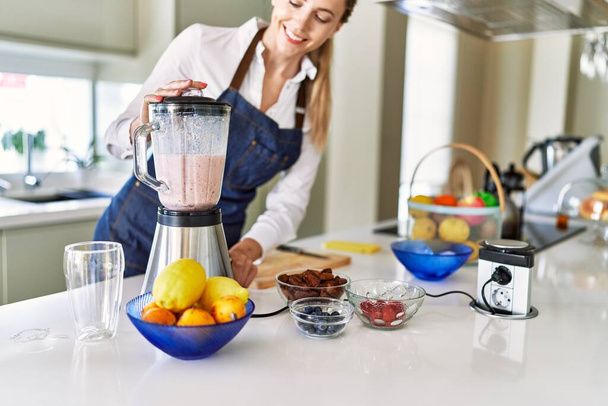 Young blonde woman smiling confident liquefying smoothie using bender at kitchen - Fotoğraf, Görsel