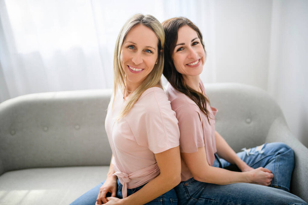 Two smiling best girl friends blond and brunette sit on sofa - Фото, зображення