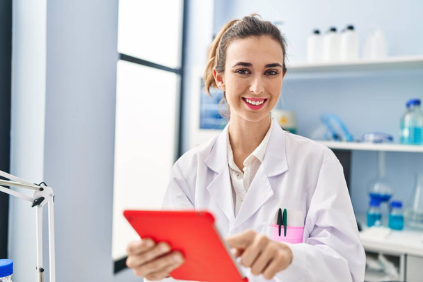 Young woman wearing scientist uniform using touchpad at laboratory - Foto, Imagen