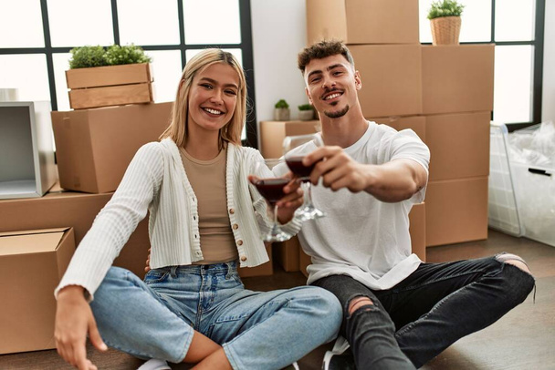Young caucasian couple toasting with red wine glass sitting at new home. - Photo, Image