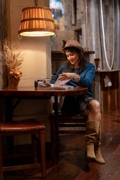 Красивый турист в шляпе и с фотоаппаратом, пьющий чай в кафе, читающий книгу, сидящую за столом - Фото, изображение