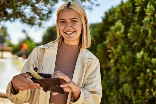Молодая блондинка улыбается счастливая, держа бумажник с банкнотами norway krone в городе. - Фото, изображение