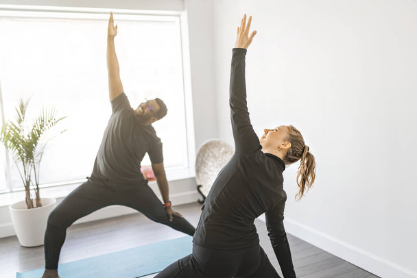 Personal trainer doing yoga pose in sunny studio with client - Fotoğraf, Görsel