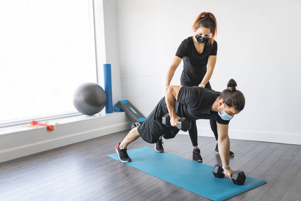 Trainer and client discussing her progress at the gym with mask - Foto, afbeelding
