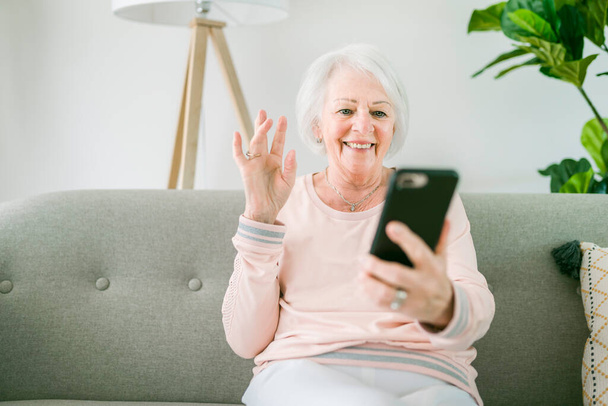 portrait of elderly woman sit on the sofa at home with cellphone - Foto, afbeelding