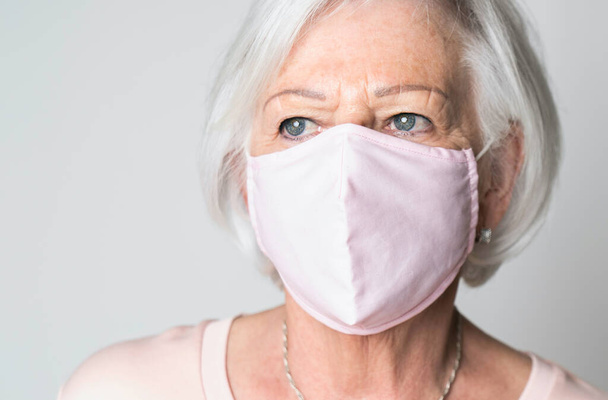 nice portrait of a retired senior woman on studio background wearing pink covid mask - Photo, Image