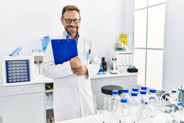 Middle age hispanic man smiling confident wearing scientist uniform at laboratory - Foto, afbeelding