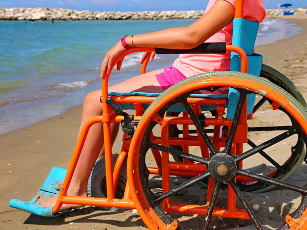 girl in a wheelchair with wheels modified to move on the sandy beach by the sea - Foto, Imagem