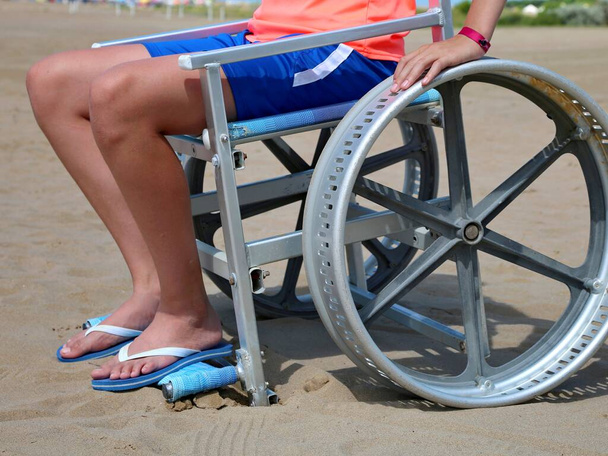 boy on the special wheelchair with big wheel in metal on the beach - Photo, Image