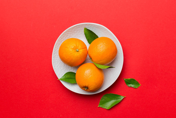 Płaskie układanie świeżych owoców pomarańczy z plasterkami w talerzu na kolorowym tle. Widok z góry z miejsca kopiowania. - Zdjęcie, obraz