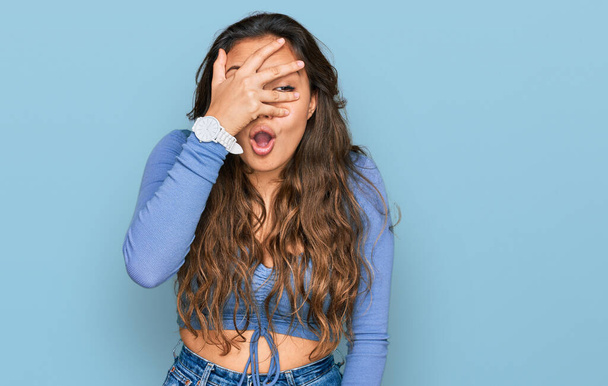Young hispanic girl wearing casual clothes peeking in shock covering face and eyes with hand, looking through fingers with embarrassed expression.  - Foto, Imagem