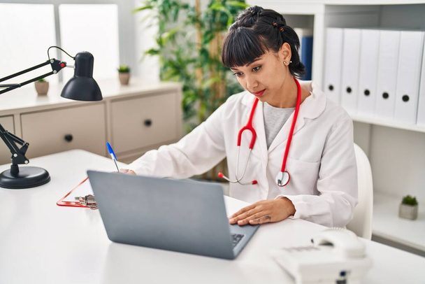 Młoda kobieta w mundurze lekarza używająca laptopa w klinice - Zdjęcie, obraz