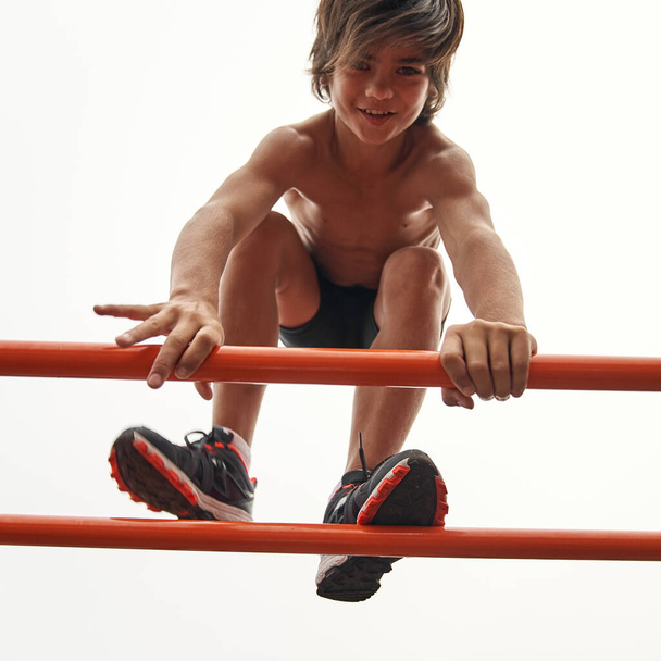 Bottom view of sports boy going on horizontal bar - Fotó, kép