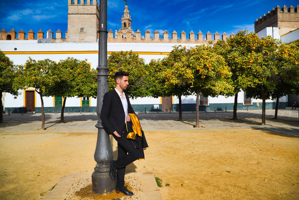 Portrait of young and handsome gipsy man, dressed in black and red shoes dancing with a black and yellow bullfighter's cape in the streets of seville. Flamenco cultural heritage of humanity. - Photo, Image