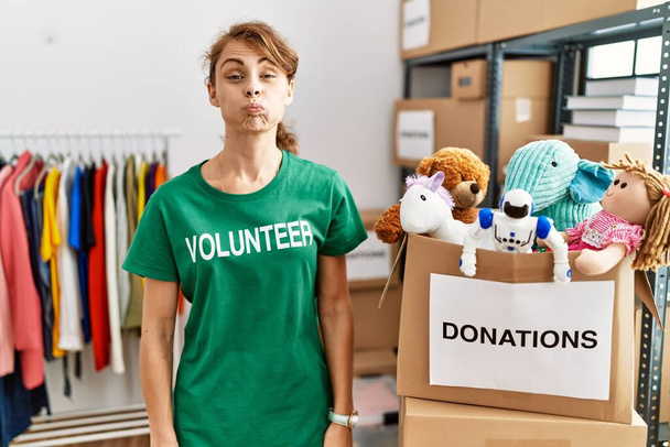 Beautiful caucasian woman wearing volunteer t shirt at donations stand puffing cheeks with funny face. mouth inflated with air, crazy expression.  - Foto, Imagem