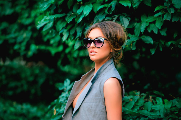 Elegante mujer fresca en traje y gafas de sol por los arbustos. Moda, estilo, concepto de tendencias - Foto, imagen