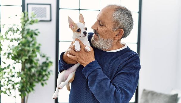 Senior grey-haired man smiling confident holding chihuahua at home - Photo, Image