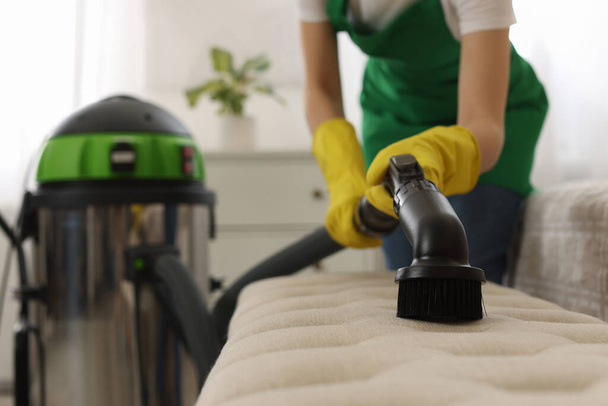 Professional janitor in uniform vacuuming furniture indoors, closeup - Фото, зображення